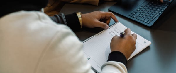 An employee writes in a notebook next to a laptop 