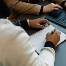 An employee writes in a notebook next to a laptop 