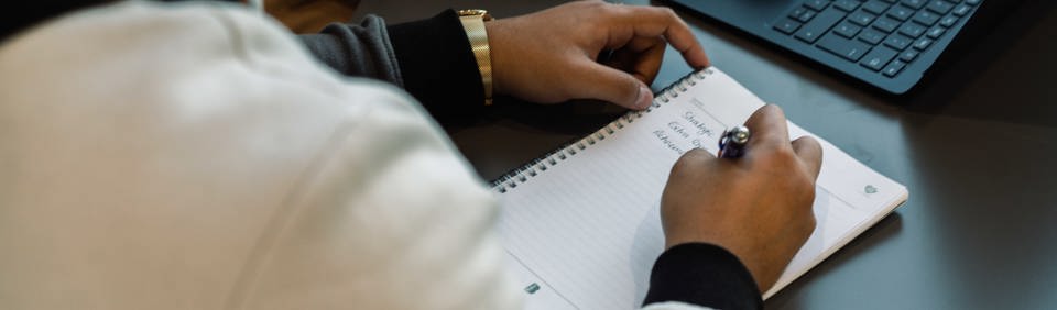 An employee writes in a notebook next to a laptop  