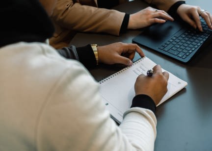 An employee writes in a notebook next to a laptop