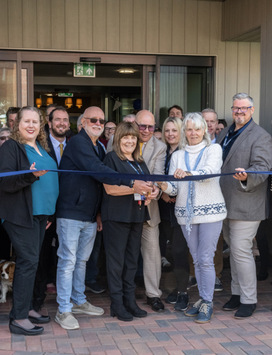 Group of residents, Housing 21 colleagues, and visitors about to cut a ribbon outside Fern Meadows 