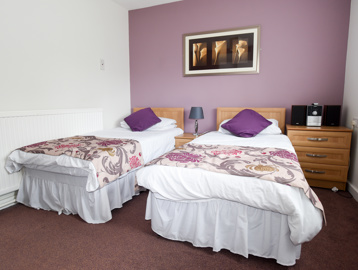 Two single beds in the guest room with side tables and stereo unit