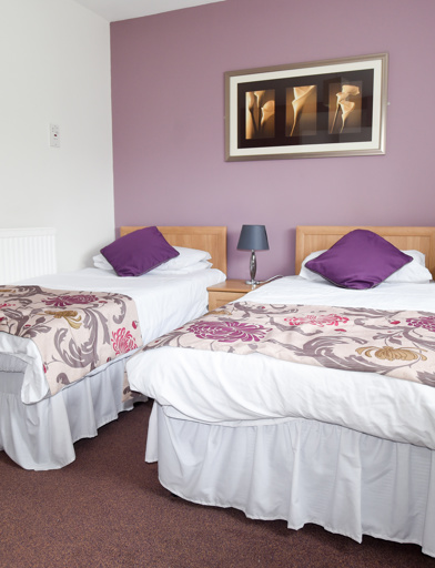 Two single beds in the guest room with side tables and stereo unit