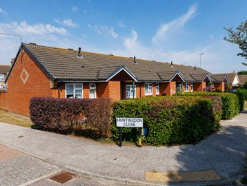 A row of bungalows set behind hedging with a footpath to the front