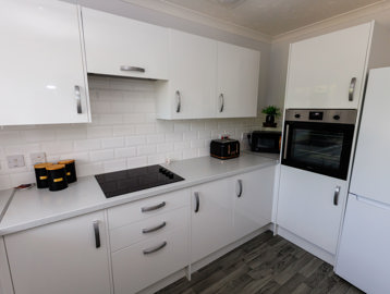 A kitchen with white units, induction hob, mid-height oven and fridge freezer