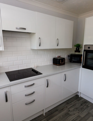 A kitchen with white units, induction hob, mid-height oven and fridge freezer 