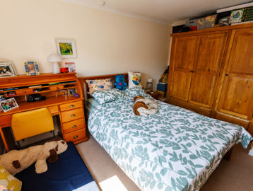 Spacious bedroom with a queen-sized bed, triple-door wardrobe, and writing desk with drawers.