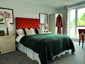 A bedroom inside an apartment at Askern Vale. Featuring a green blanket, a cream wardrobe and two bedside tables with lamps