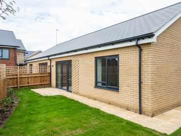 Rear of the show home bungalow with grassed garden area and small path and patio