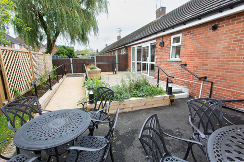 A landscaped garden with metal tables and chairs and wooden planters filled with plants.