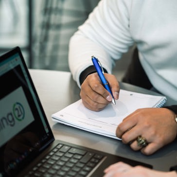 An employee writes in a notebook next to a laptop displaying the Housing 21 logo
