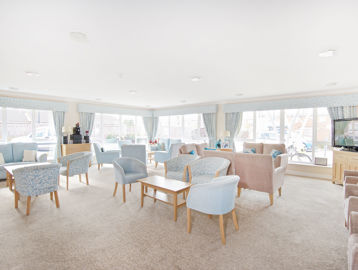 Communal lounge with soft seating and coffee tables and large TV in the corner