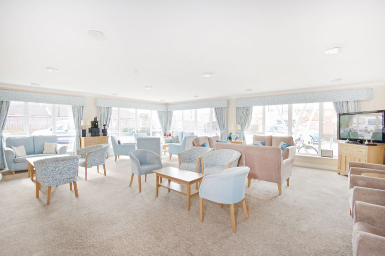 Communal lounge with soft seating and coffee tables and large TV in the corner