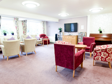 Residents' communal lounge with soft seating, tables and wall mounted TV