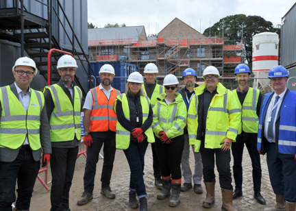 A group of colleagues from Housing 21 and partners standing in front of a new development wearing hard hats and high vis vests