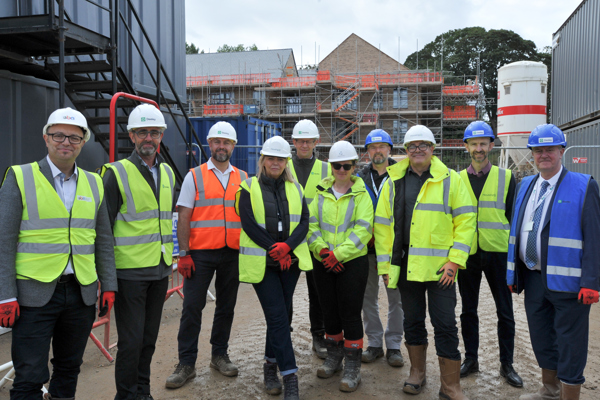 A group of colleagues from Housing 21 and partners standing in front of a new development wearing hard hats and high vis vests