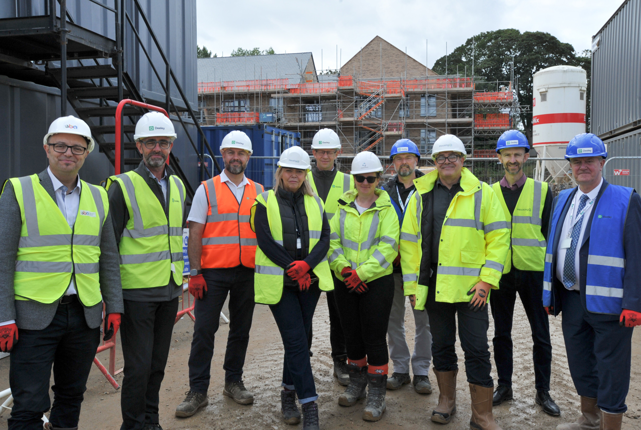 A group of colleagues from Housing 21 and partners standing in front of a new development wearing hard hats and high vis vests