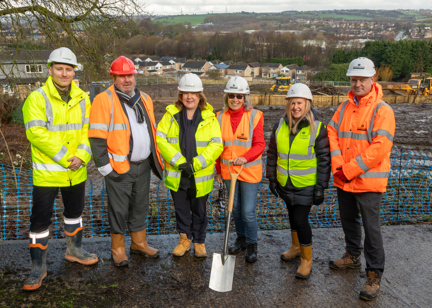 Key representatives from Housing 21, Kirklees Council, and Robertson Group, standing outside in high vis jackets and hard hats holding a spade at the Cleckheaton Extra Care scheme ground-breaking ceremony