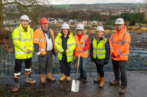 Key representatives from Housing 21, Kirklees Council, and Robertson Group, standing outside in high vis jackets and hard hats holding a spade at the Cleckheaton Extra Care scheme ground-breaking ceremony