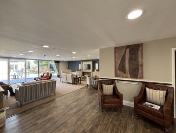 Open plan communal lounge featuring brown wooden flooring that meets carpet with sofa's and arm chairs around the room