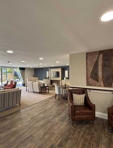 Open plan communal lounge featuring brown wooden flooring that meets carpet with sofa's and arm chairs around the room 