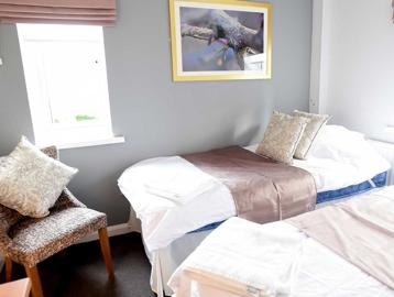 A stylish bedroom with two single beds, and a single chair, with cushions