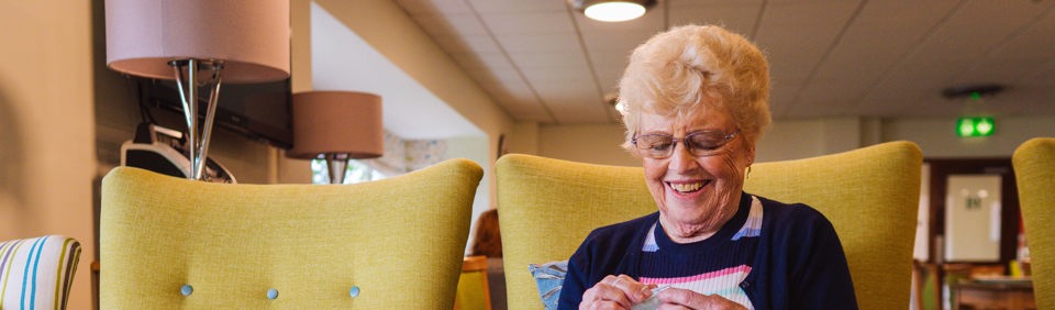 A resident sitting down knitting 