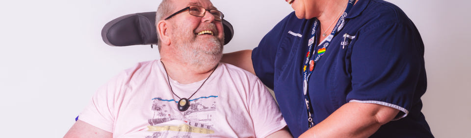 Resident in a wheelchair smiling with their care worker in a studio-style photoshoot 
