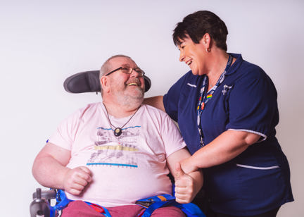 Resident in a wheelchair smiling with their care worker in a studio-style photoshoot