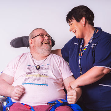 Resident in a wheelchair smiling with their care worker in a studio-style photoshoot