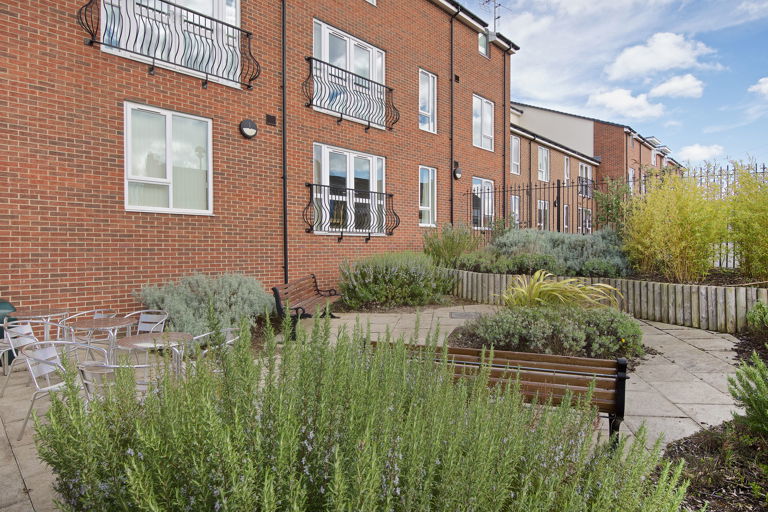 Large patio area with tables, chairs and benches surrounded by plants and shrubs