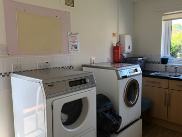 Two washing machines in a laundry room with a sink and bin in the room