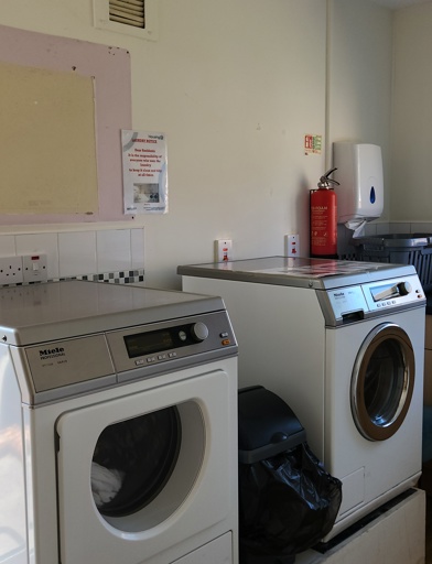 Two washing machines in a laundry room with a sink and bin in the room 