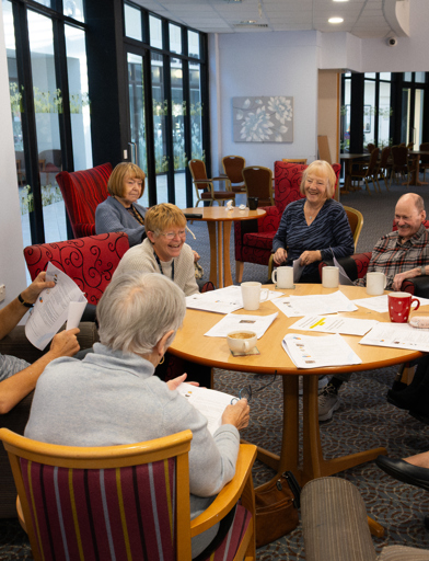 A group of residents sat around a table smiling and laughing enjoying a quiz 