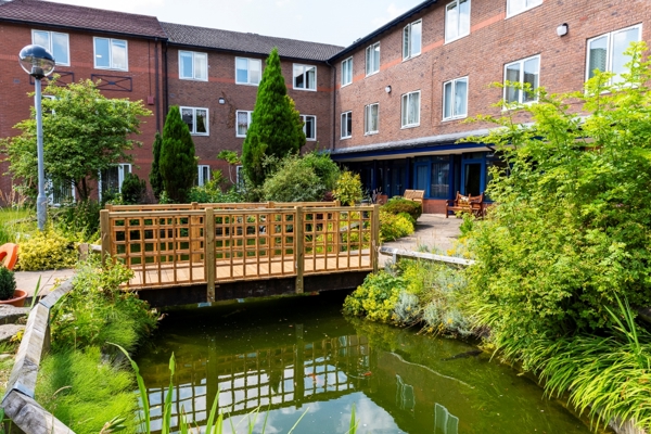 A three storey residential property overlooks a pond with a bridge across it