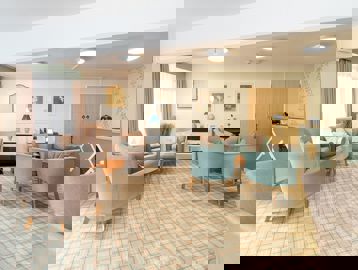 Residents' lounge with soft seating and coffee tables and small communal kitchen area