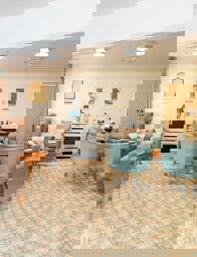 Residents' lounge with soft seating and coffee tables and small communal kitchen area