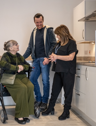 Female resident in wheelchair with a young male, laughing with a local manager when in a scheme kitchen 