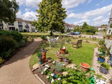 A garden on a sunny day featuring planted flowers, tree's, grass and garden furniture 
