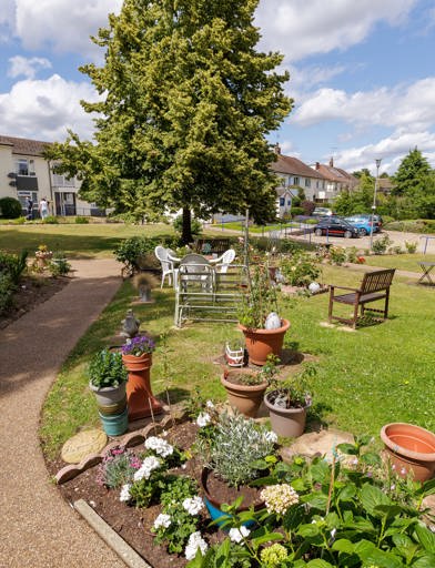 A garden on a sunny day featuring planted flowers, tree's, grass and garden furniture  