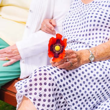 The arms of two ladies sitting on a bench and one holds a flower