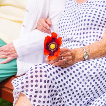The arms of two ladies sitting on a bench and one holds a flower