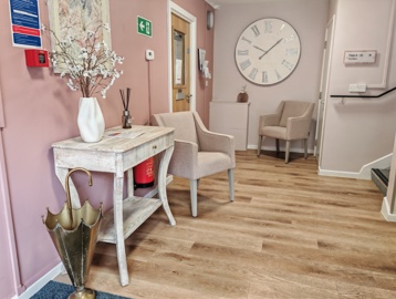 An armchair and small desk in a waiting area with pink walls, and a wooden floor