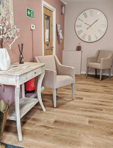 An armchair and small desk in a waiting area with pink walls, and a wooden floor 