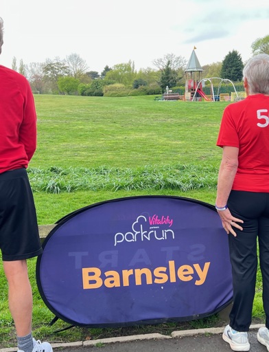 Judith looking at a field and park with a Barnsley Park Run sign in the centre. 