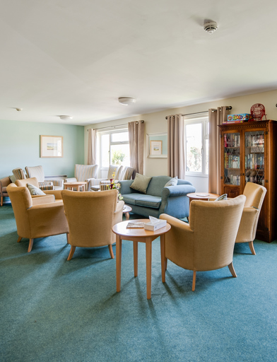 Residents' lounge with soft seating and coffee tables and a book shelf 