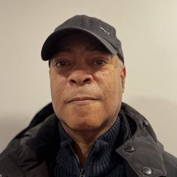 A man wearing a baseball cap, jumper and jacket smiling into the camera