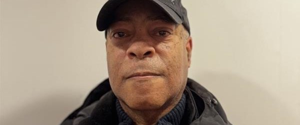 A man wearing a baseball cap, jumper and jacket smiling into the camera
