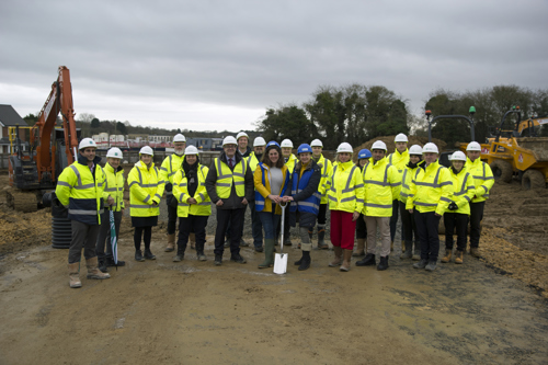 Housing 21 employees along with the Leader of Vale of White Horse Council and District councillor with key representatives stood outside on muddy ground with a spade, wearing high vis jackets and hard hats