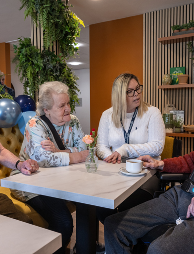 Three residents talking to a Housing 21 colleague while sat at a table in the communal lounge 